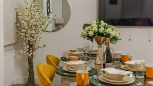A dining table set with plates, glasses, and a vase of flowers. - Luxurious 1 Bedroom on Iconic Harley Street (Greater London)