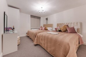 A hotel room with two beds, a minibar, a mirror, and a chandelier.