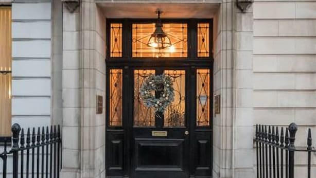 A building entrance with a black door, a decorative wreath, and a light fixture above the door. - Luxurious 1 Bedroom on Iconic Harley Street (Greater London)