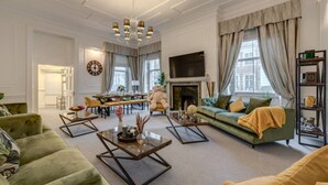 A spacious living room with a fireplace, green sofa, and a dining area with a chandelier.