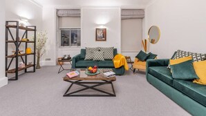 A living room with a green sofa, a yellow sofa, a coffee table, and a bookshelf. - Modern Elegance: 1-Bedroom City Living in London (Greater London)
