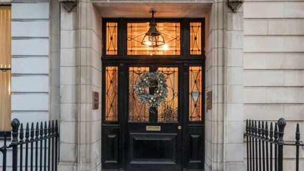 A building entrance with a black door, a decorative wreath, and a light fixture above the door. - Modern Elegance: 1-Bedroom City Living in London (Greater London)