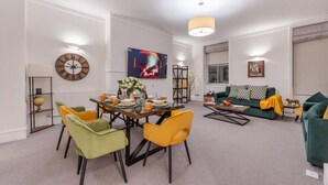 A modern living room with a dining area, featuring a round table, colorful chairs, a sofa, and a television. - Modern Elegance: 1-Bedroom City Living in London (Greater London)