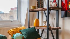 A corner room with a yellow armchair, a green and yellow cushion, and a black metal shelving unit against the wall.