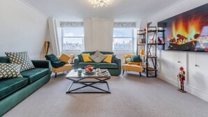 A living room with a green sofa, a yellow armchair, a coffee table, and a TV on the wall.