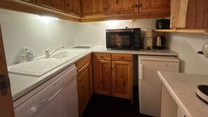 A compact kitchen with wooden cabinets, a microwave, a coffee maker, and a dishwasher.