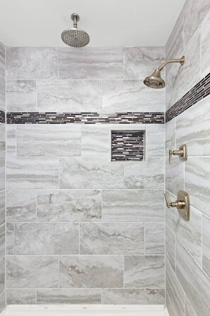 A shower with a rain showerhead, a handheld showerhead, and a wall-mounted control.