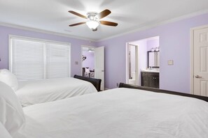 A bedroom with two beds, a ceiling fan, and a bathroom visible through an open door.