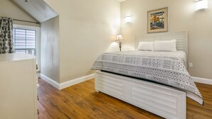 Una camera da letto con un letto, un comodino, una lampada, un quadro appeso al muro e una finestra con tende.