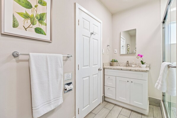 A bathroom with white cabinets, a sink with a marble countertop, a framed botanical print on the wall, and a towel rack with a white towel.