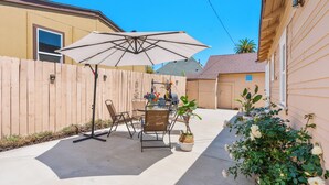 Ein Hinterhof-Terrasse mit Tisch, Stühlen, einem großen Sonnenschirm und Topfpflanzen.