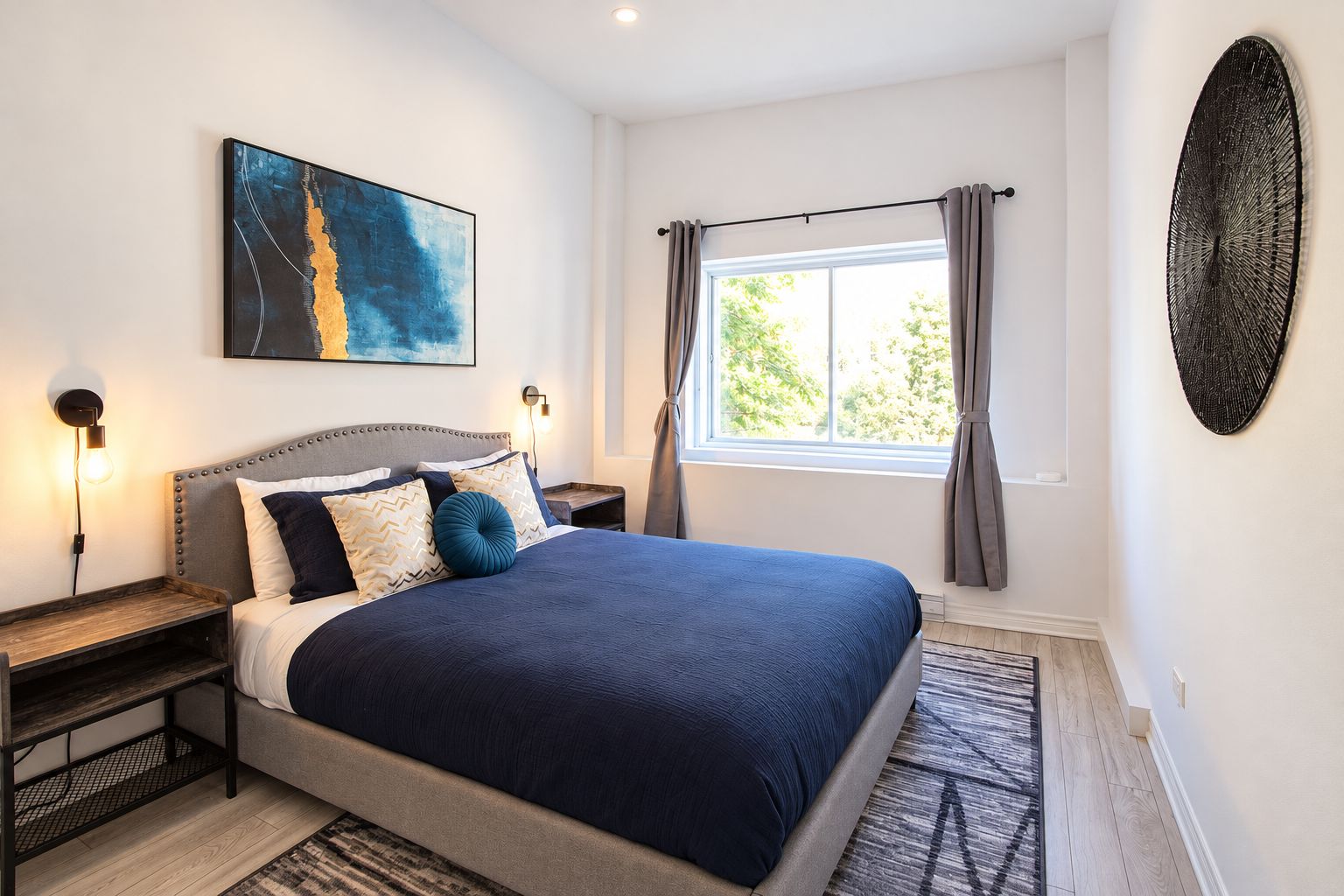 A bedroom with a large bed, a nightstand, a wall-mounted artwork, a window with curtains, and a textured wall decoration.