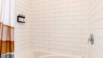 Un baño moderno con una bañera independiente, paredes cubiertas de azulejos blancos y un cabezal de ducha.