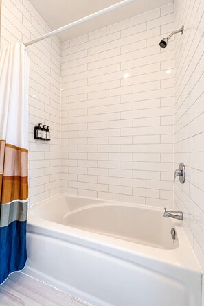 Une salle de bain moderne avec une baignoire sur pieds, des murs recouverts de carreaux blancs et une pomme de douche.