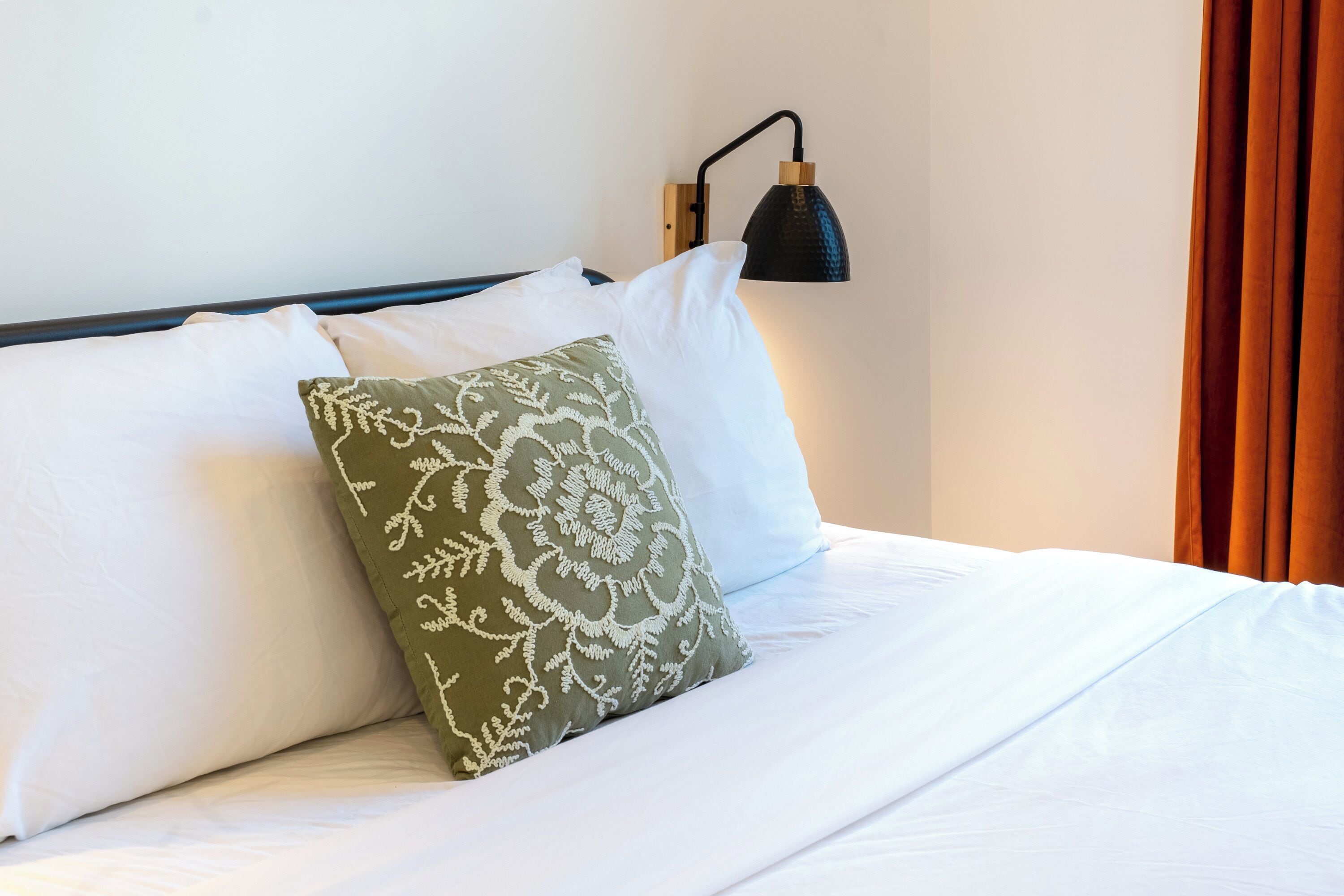 A neatly made bed with white linens and a green patterned pillow.