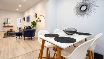 Un salon moderne avec un coin repas, comprenant une table blanche avec des sets de table noirs, un canapé bleu et un grand miroir décoratif mural.