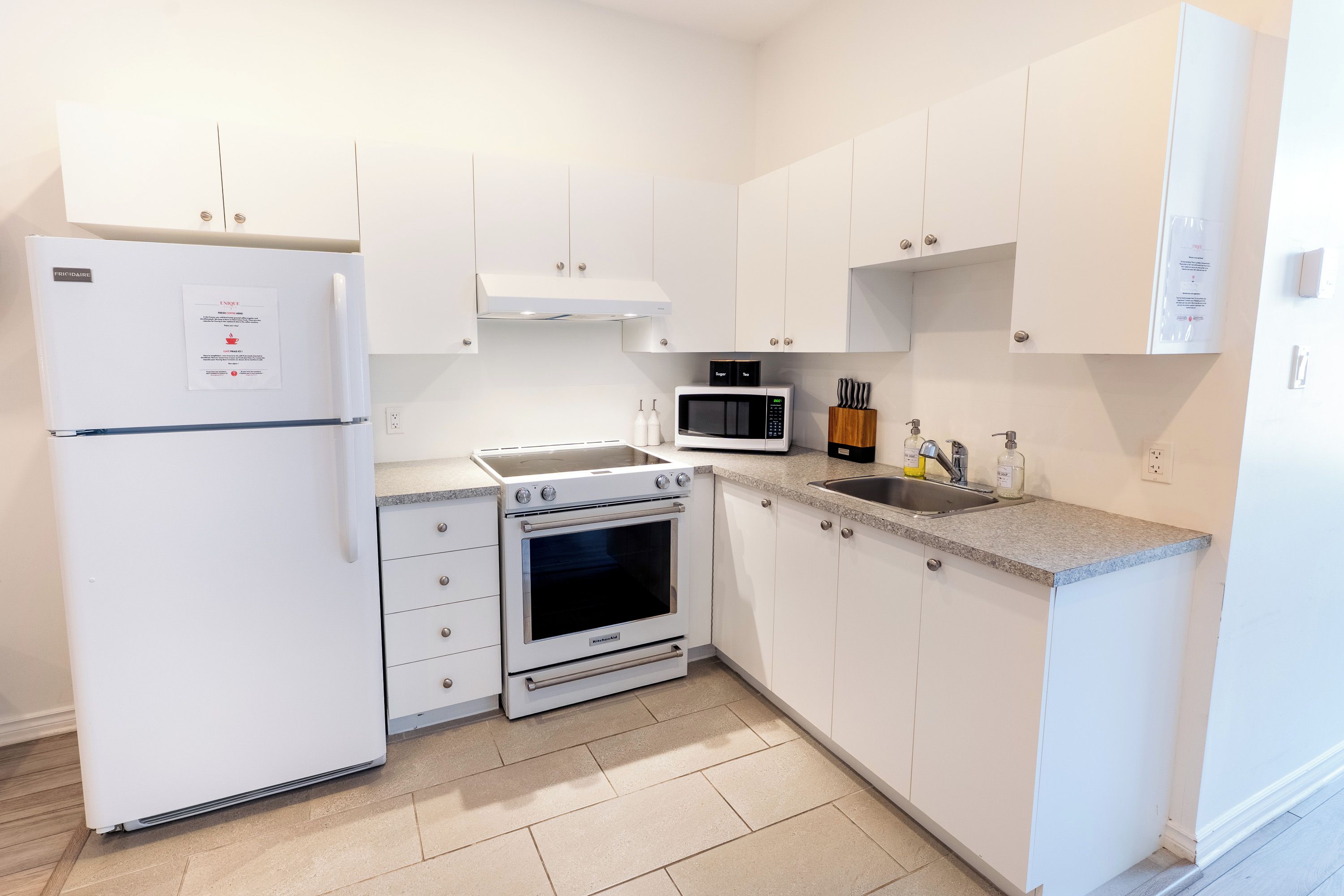 Une cuisine moderne avec des meubles blancs, un four encastré, un four à micro-ondes et un réfrigérateur.