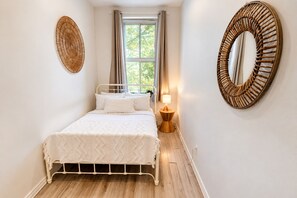 Une chambre à coucher comprenant un lit, une table de chevet avec une lampe, une fenêtre avec des rideaux et deux éléments décoratifs fixés au mur.