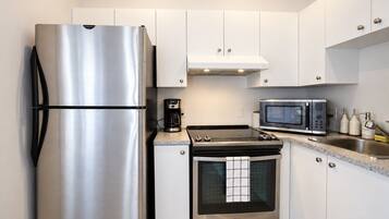 A compact kitchen with a stainless steel refrigerator, a coffee maker, a microwave, and an oven.