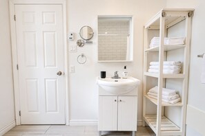 Une salle de bain avec une porte blanche, un lavabo surmonté d’un miroir et un porte-serviettes avec des serviettes pliées.