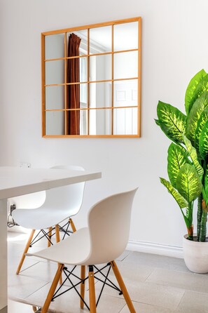 Un espace repas moderne avec une table blanche, deux chaises blanches et une grande plante en pot.