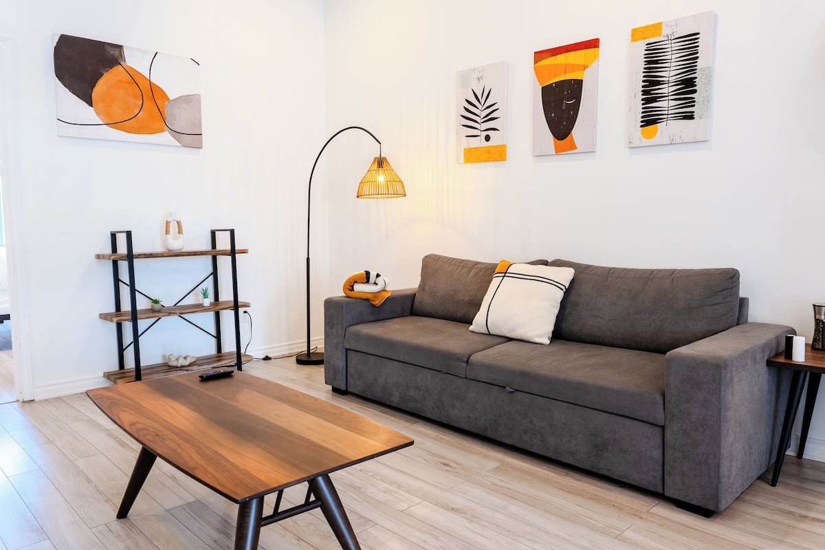 A modern living room with a grey sofa, wooden coffee table, and abstract wall art.