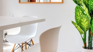 A modern dining area with a white table, two white chairs, and a large potted plant. - Unique Stays - 3658 Boul. Saint-Laurent (Montreal)