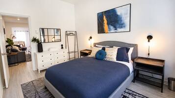 A modern bedroom with a large bed, bedside tables, a dresser, a mirror, and a painting on the wall.