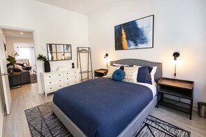 Une chambre à coucher moderne avec un grand lit, des tables de chevet, une commode, un miroir et un tableau accroché au mur.
