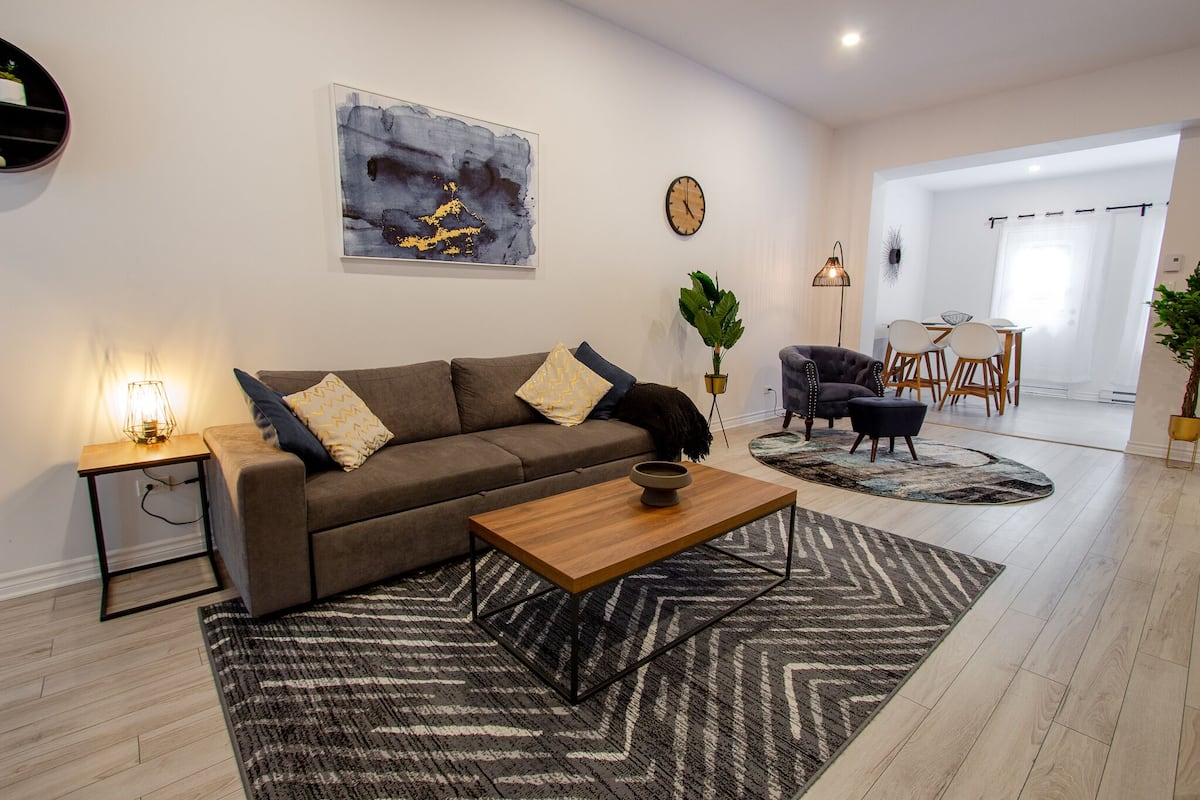 A modern living room with a sofa, coffee table, and a dining area with chairs and a table.