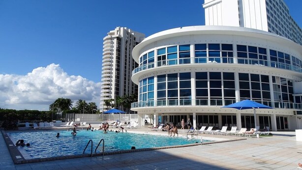 Un hotel con piscina, sillas de descanso y un edificio alto al fondo.
