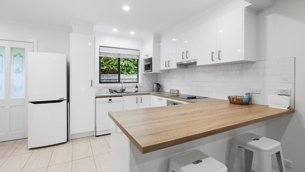 Una cocina moderna con armarios blancos, encimera de madera y ventana con vistas a zonas verdes.