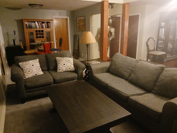 A living room with two grey sofas, a wooden coffee table, a lamp, and a bookshelf.