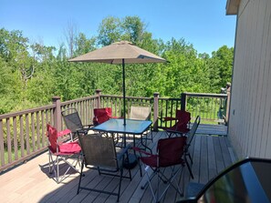 A wooden deck with a table and chairs, a covered umbrella, and a view of a green forest.