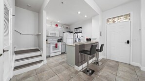 Una cocina moderna con armarios blancos, una isla central y una escalera que sube a un segundo piso.