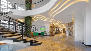 Um hall de hotel moderno com piso de mármore, escadaria, área de estar com assentos verdes e balcão de recepção.