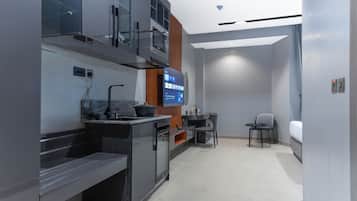 Una cocina moderna con horno empotrado, microondas y una pantalla digital que muestra un menú. Hay un comedor con mesa y sillas, y una pequeña zona de estar con sofá.