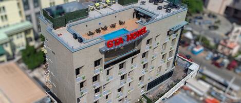 Un edificio de varios pisos con piscina en la azotea y zona de estar al aire libre, con el rótulo "GTA Hotel".