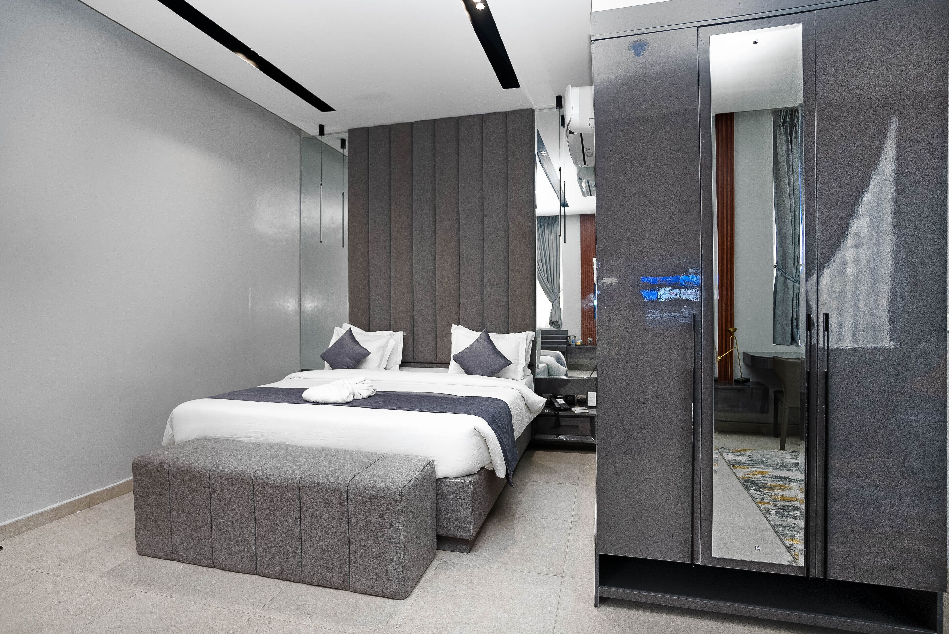Een moderne slaapkamer met een groot bed, een grijze bank, een garderobe en een spiegel.