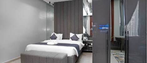 Un dormitorio moderno con una cama grande, un banco gris, un armario y un espejo.