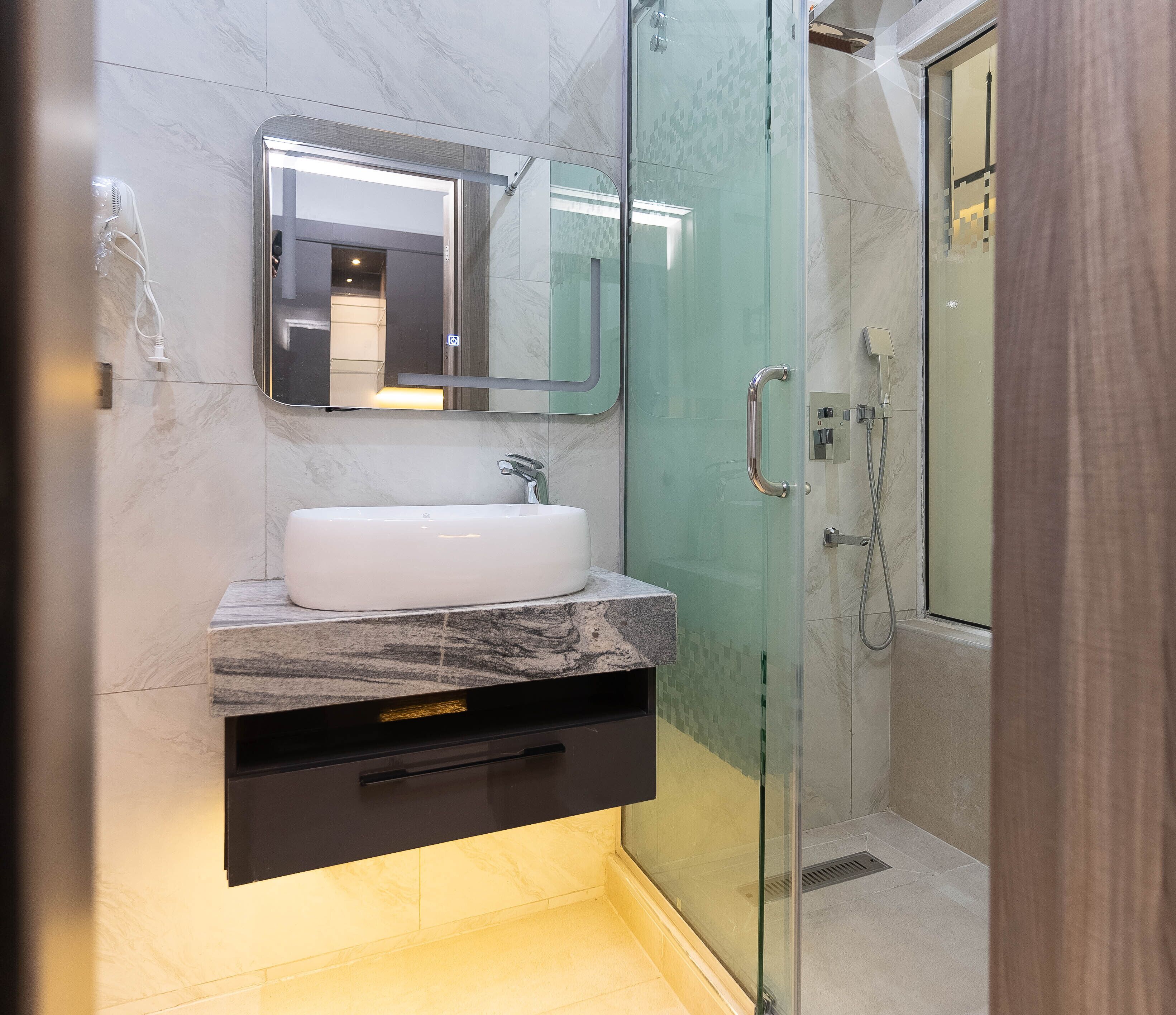 A modern bathroom with a glass-enclosed shower, a white sink, and a marble countertop.