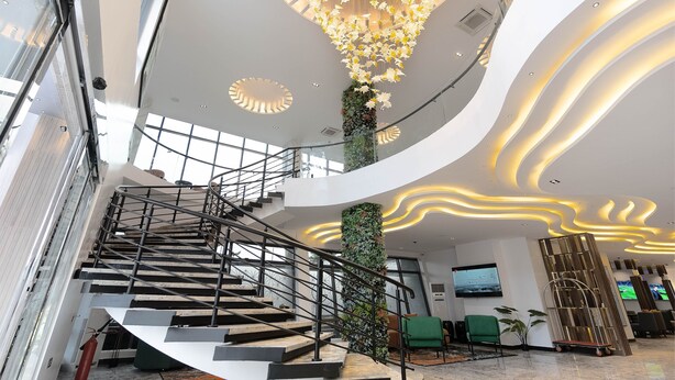 Um hall de hotel moderno com uma escadaria central, um lustre grande e uma área de estar.