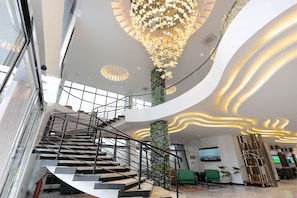 A modern hotel lobby with a central staircase, a large chandelier, and a seating area. - GTA Hotel Ikeja (Lagos)