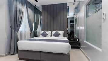 A modern bedroom with a large bed, grey curtains, and a glass partition on one side.