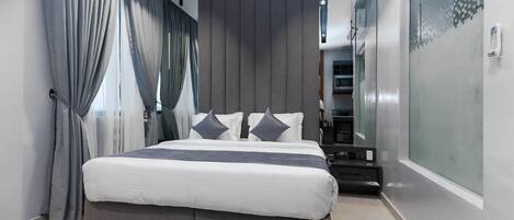 A modern bedroom with a large bed, grey curtains, and a glass partition on one side.