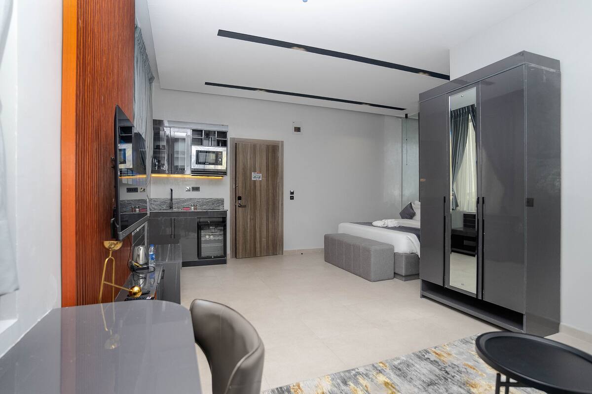 A modern hotel room with a dining area, kitchenette, and a large wardrobe.