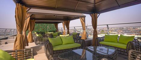 An outdoor seating area with wicker furniture and green cushions, a glass table, and a view of the cityscape.