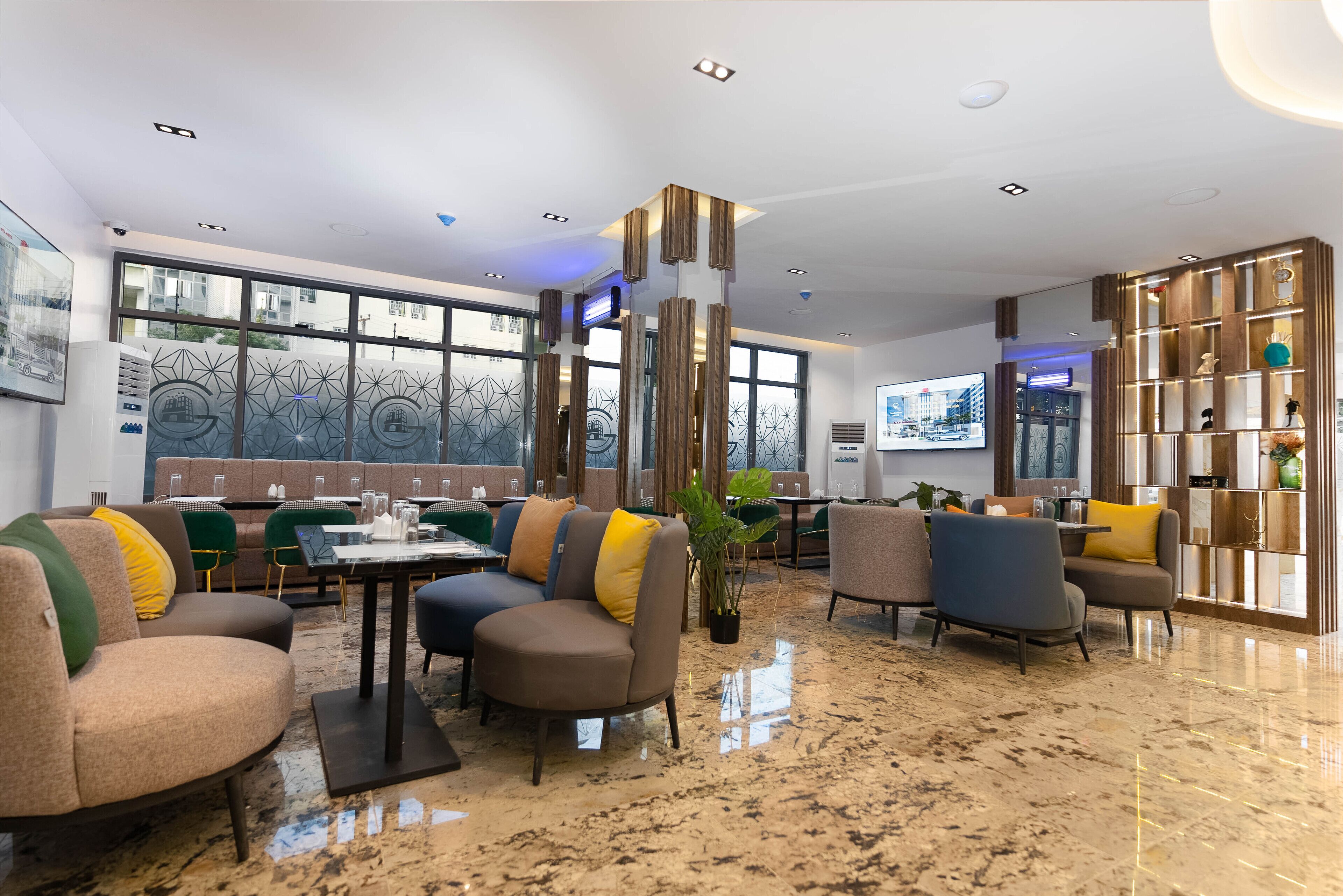 A modern lounge area with seating, a coffee machine, and a large window with a city view.