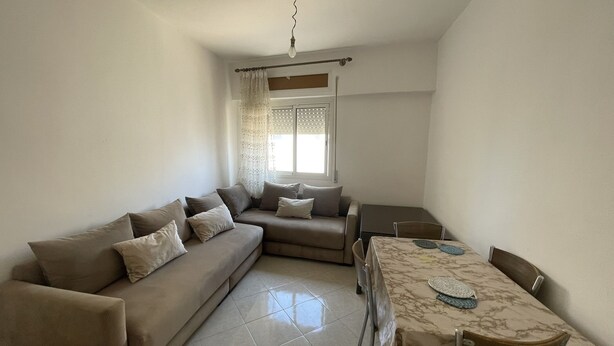 A living room with a sofa, a dining table with chairs, and a window with curtains.