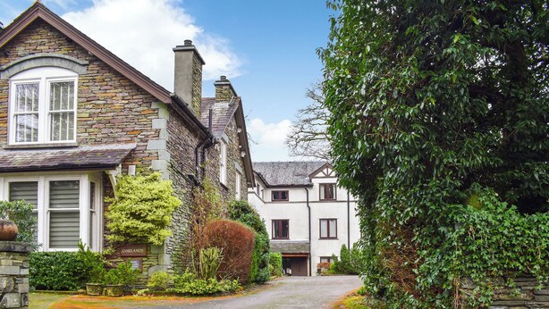 A stone building with a white facade and a traditional design, featuring a driveway leading to a gated entrance. - 2 bedroom accommodation in Ambleside (Ambleside)